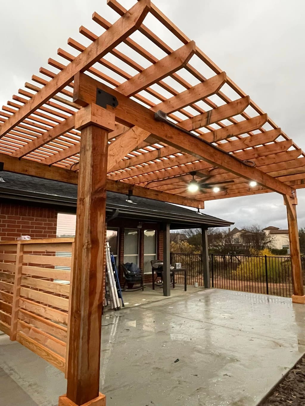 Open-slat cedar pergola with heavy timber posts and steel bracket connections over a poured concrete patio