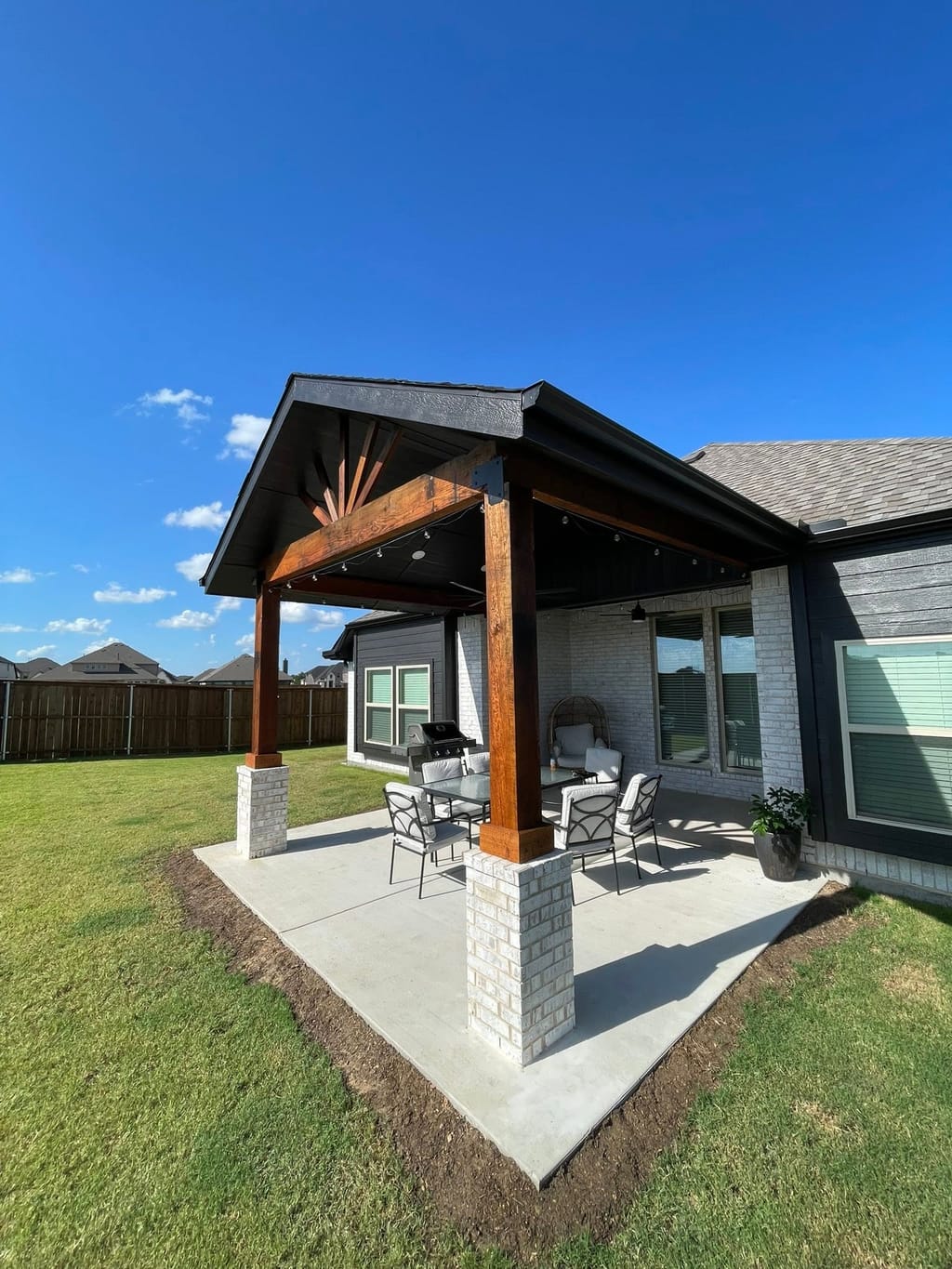 Attached patio cover with stained cedar beams and brick column bases over a new concrete slab