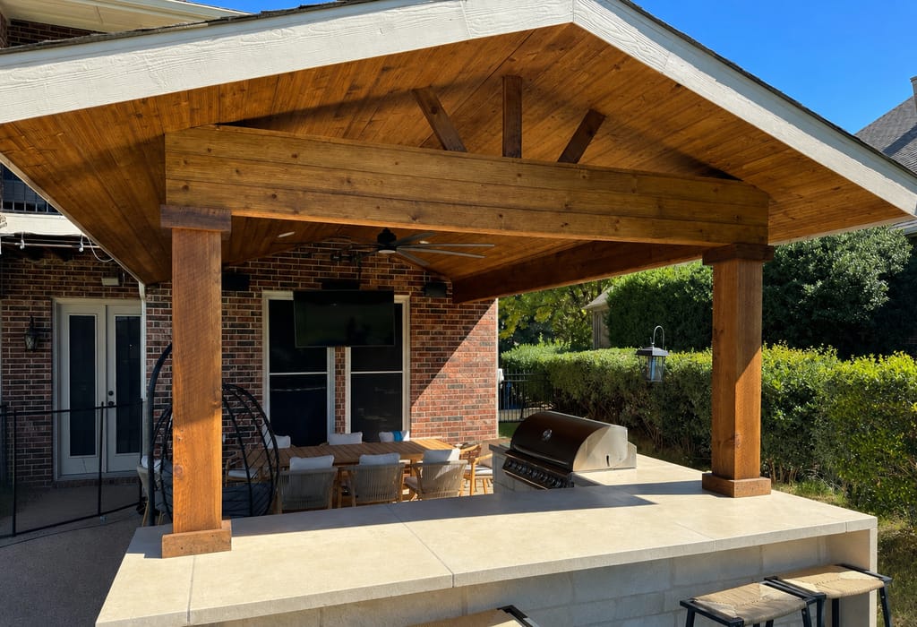 Cedar gable patio cover over an outdoor kitchen with a built-in grill, stone bar and mounted television