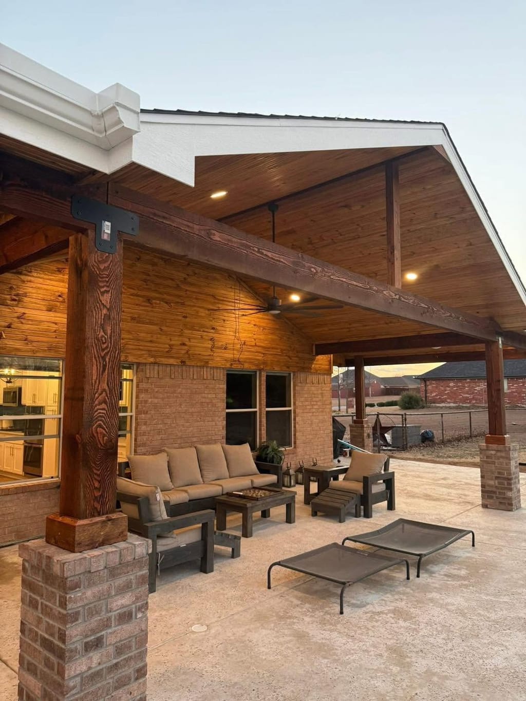 Vaulted cedar patio cover lit at dusk over a seating area with brick column bases