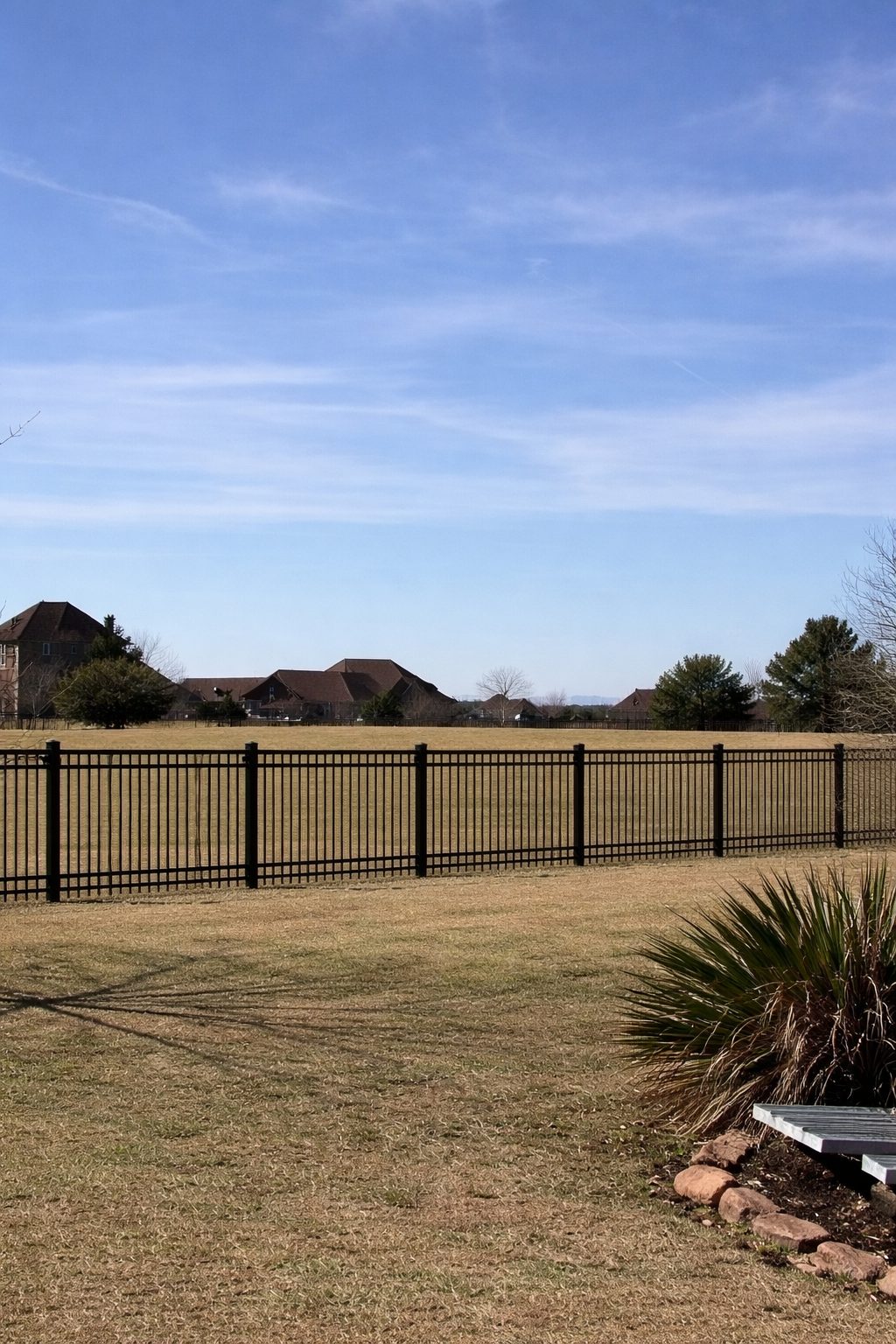 Black wrought iron ranch-style fence bordering an open field